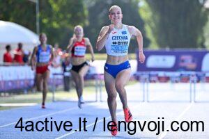 Botkova - 4Active - 4Active Young female sprinter in blue Czechia kit finishing a race on a blue track, giving a thumbs-up with a smile. Behind her, other runners and spectators blur in the background.