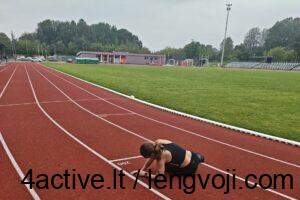 Athlete performing a push-up on a red running track beside a green field at a stadium.